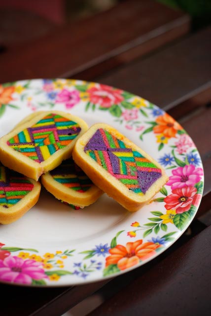 A multicoloured cake called a kek lapis Sarawak on a floral plate on a dark wood table