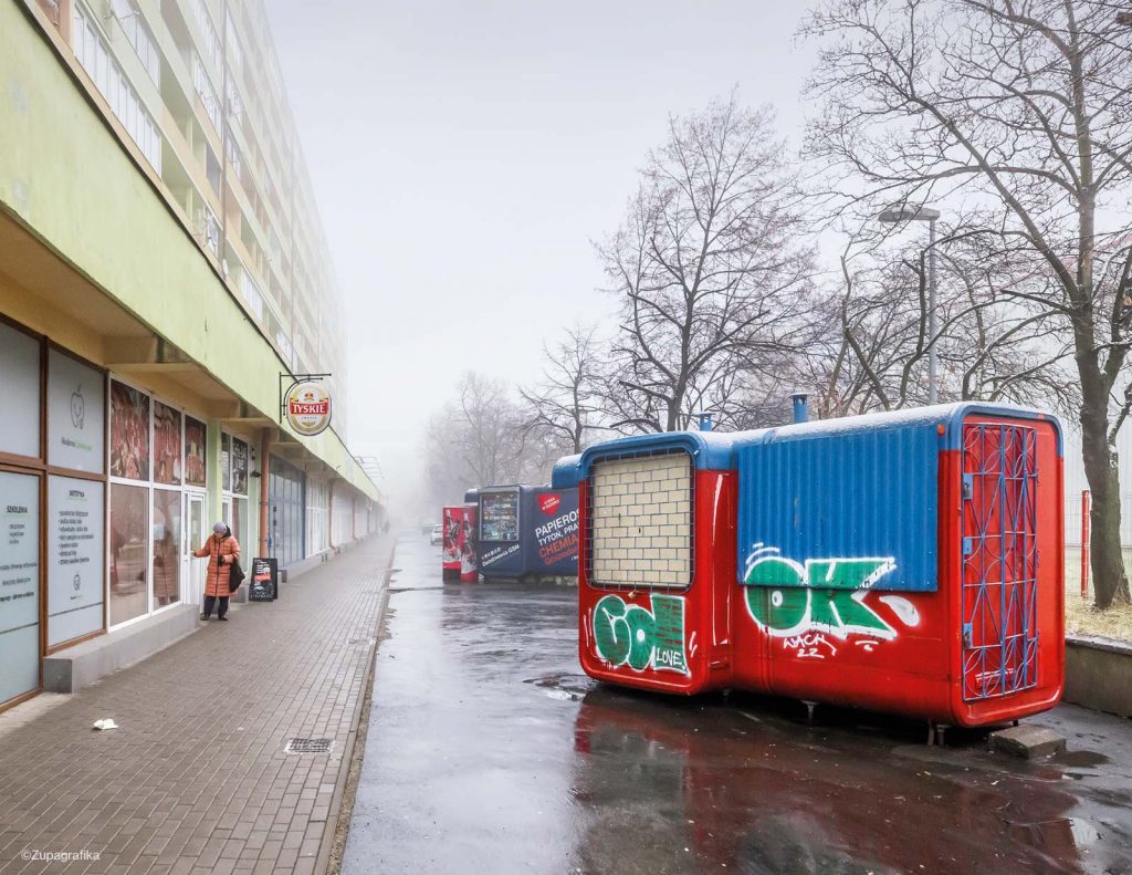 a red and blue kiosk in a wet polish street